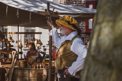 Man in ouderwetse Hanze-kledij voor een kraam met spullen uit de Hanzetijd, in Doesburg tijdens het jaarlijkse Hanzefeest